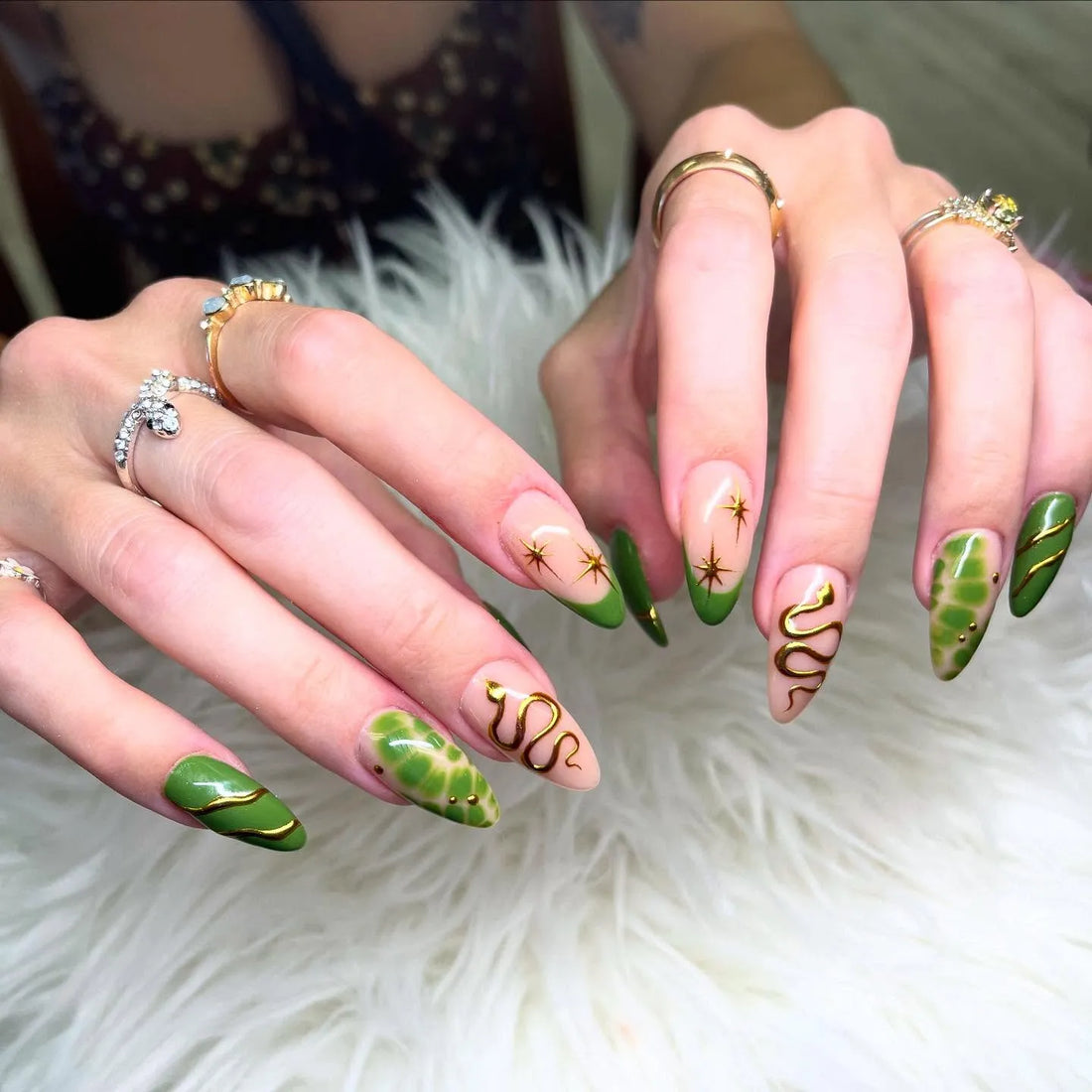 Hand with handmade forest green press-on nails featuring gold snake, star, and celestial designs