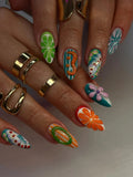 Hand with long, colorful press-on nails featuring abstract, floral, and fruity summer designs.