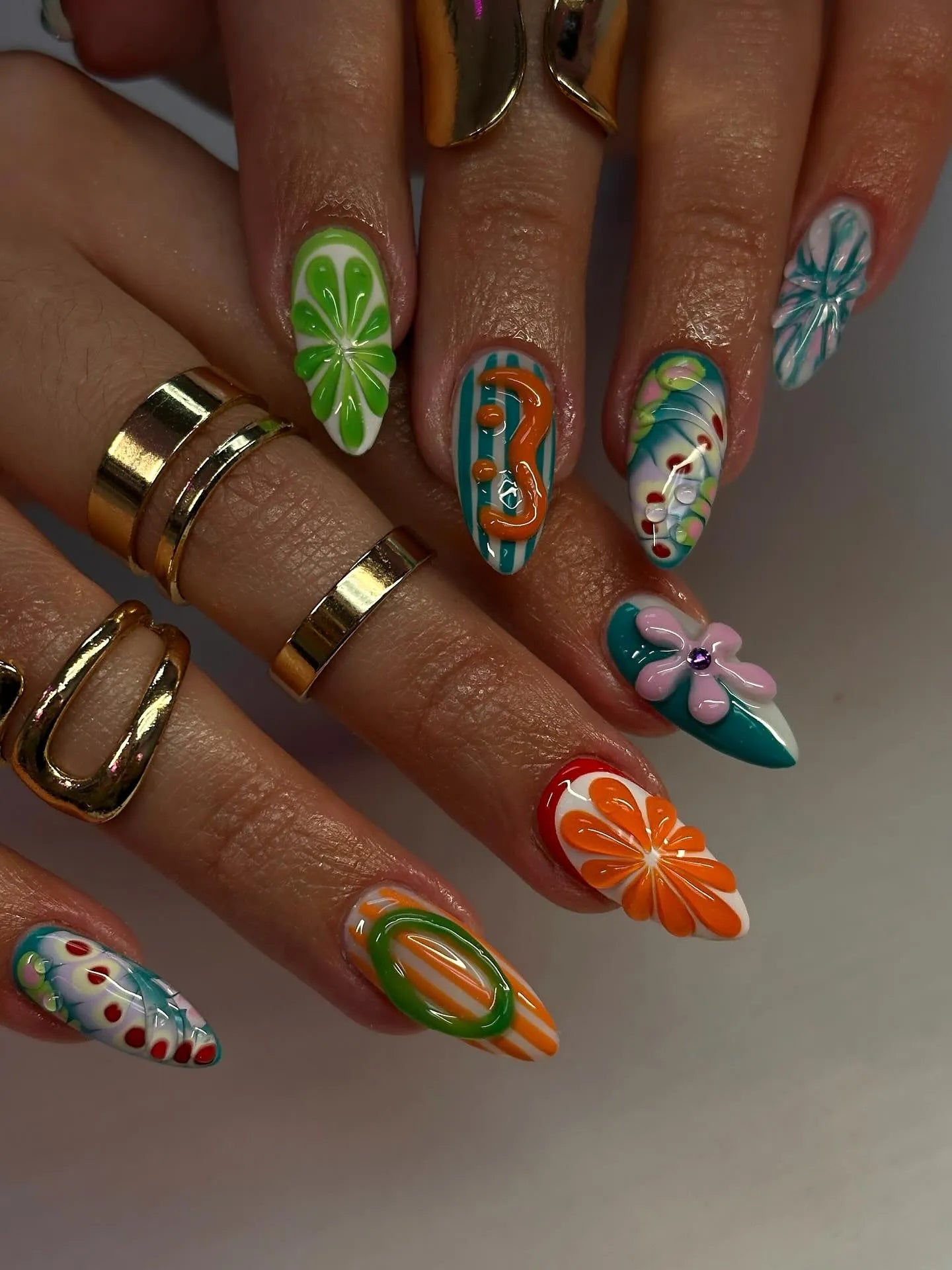 Hand with long, colorful press-on nails featuring abstract, floral, and fruity summer designs.