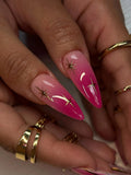 Hand with long almond-shaped hot pink ombre press-on nails featuring gold star accents.