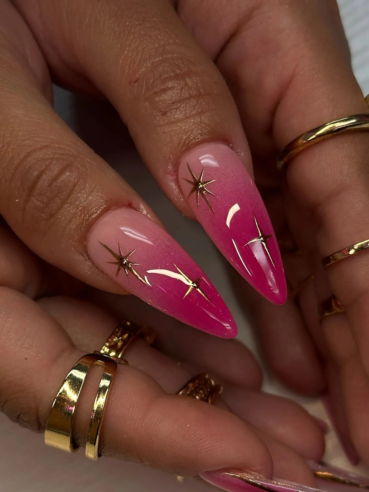 Hand with long almond-shaped hot pink ombre press-on nails featuring gold star accents.