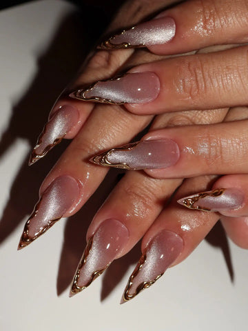 Hand with long press-on nails featuring gold chrome French edges and shimmering pink design