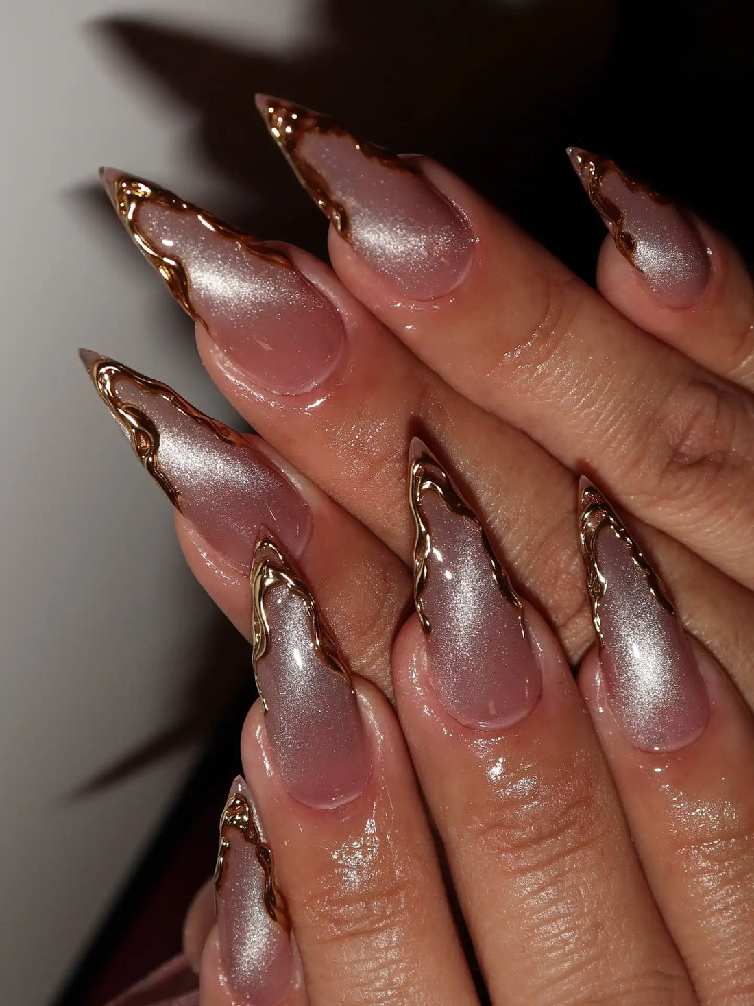 Hand with long press-on nails featuring gold chrome French edges and shimmering pink design