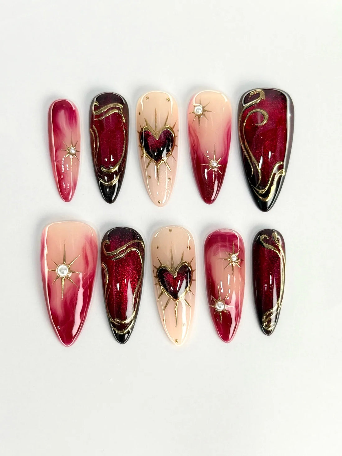 Handmade crimson ombre press-on nails with gold heart, starburst, and gem accents