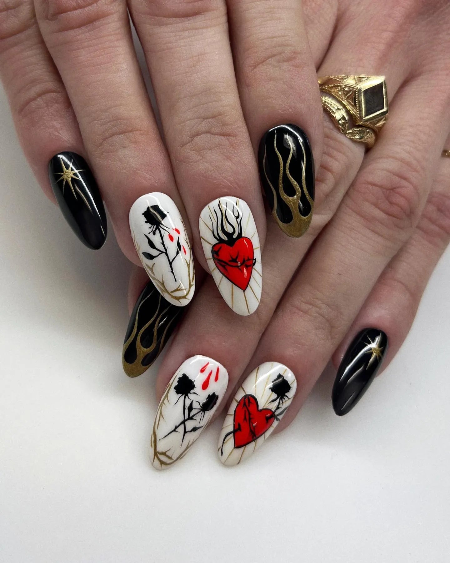 Handmade almond press-on nails with black, gold, and white designs, featuring sacred hearts, roses, flames, and stars.