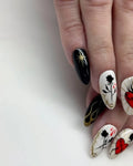 Hand with almond-shaped press-on nails featuring black, gold, and red gothic heart and rose designs.