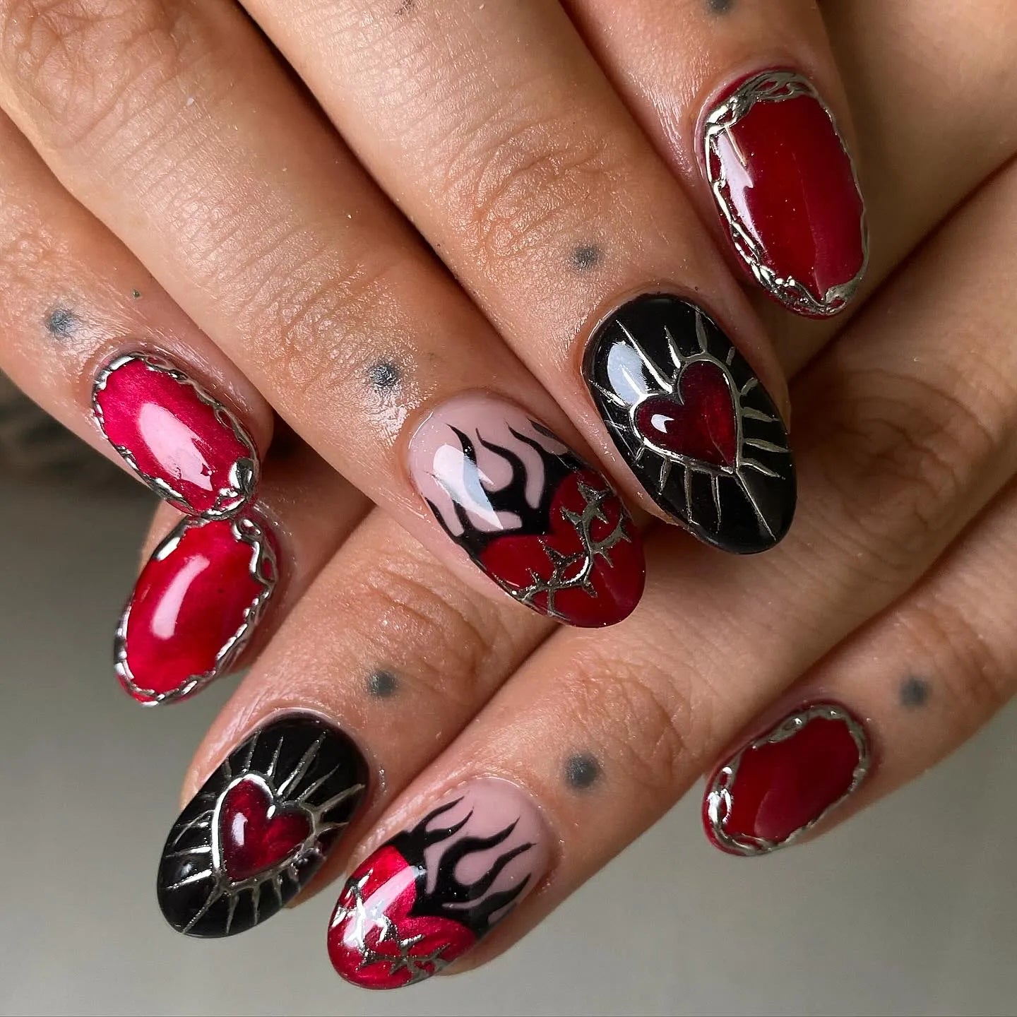 Handmade gothic press-on nails with red flames, silver chrome details, and sacred heart designs.