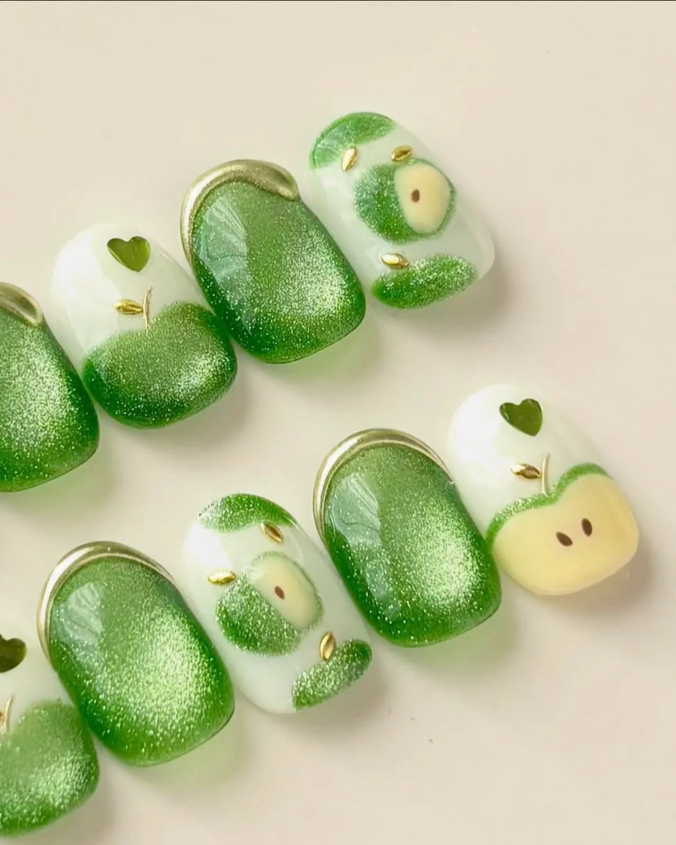 Handmade press-on nails with green apple cat eye shimmer and heart design on white base.