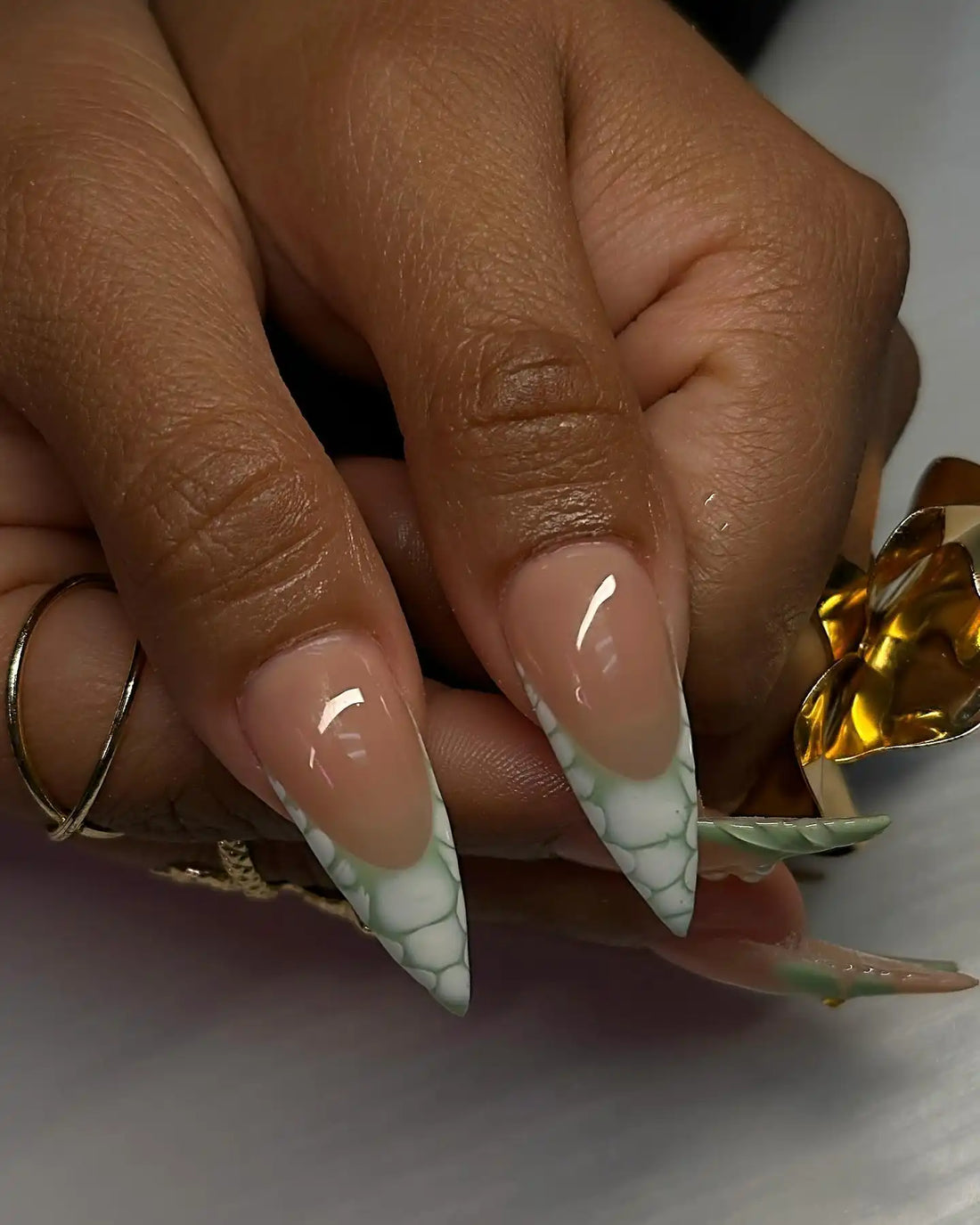 Hand with stiletto press-on nails featuring green floral accents, pearls, and crackle design tips.