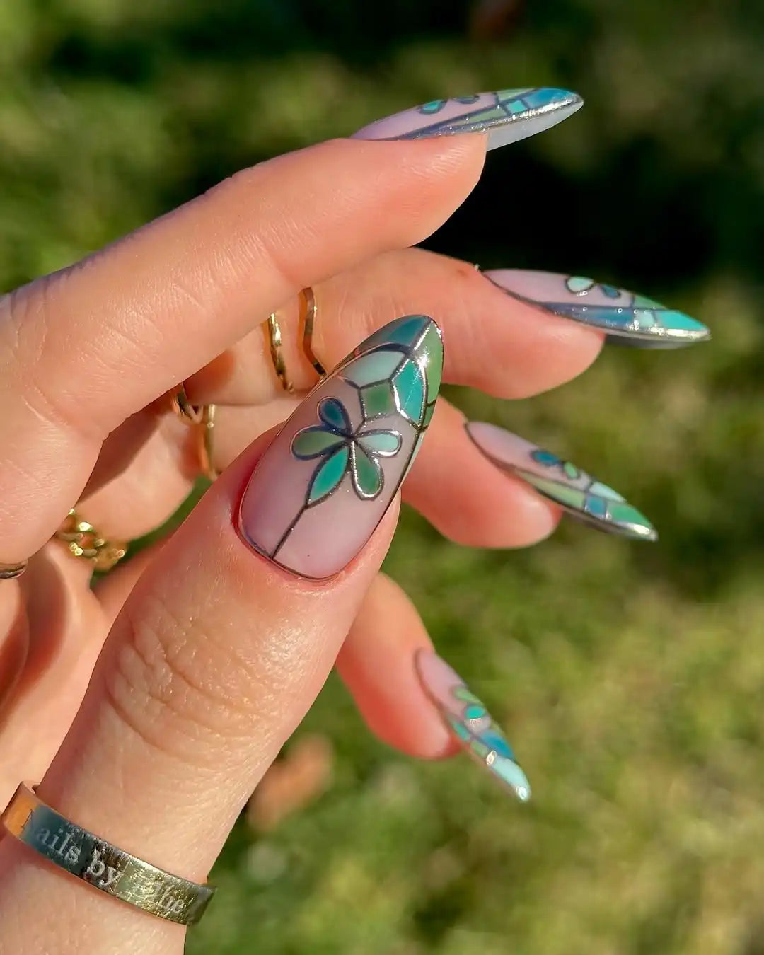 Hand holding green floral stained glass press-on nails with elegant art design outdoors