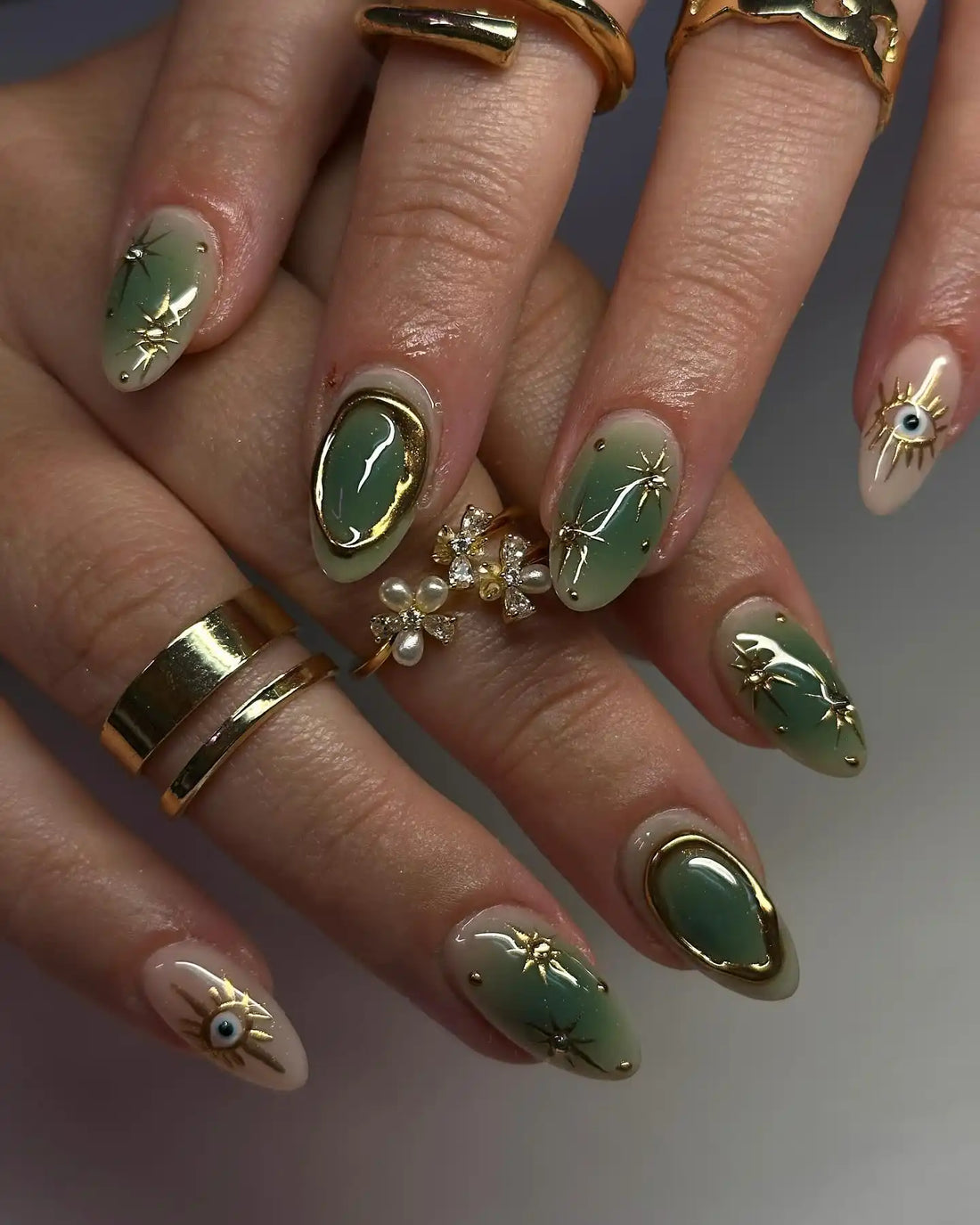 Hand with handmade green and gold celestial press-on nails featuring evil eye designs