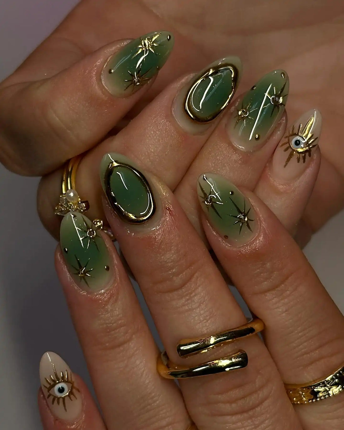 Hand with handmade green and gold celestial press-on nails featuring evil eye designs