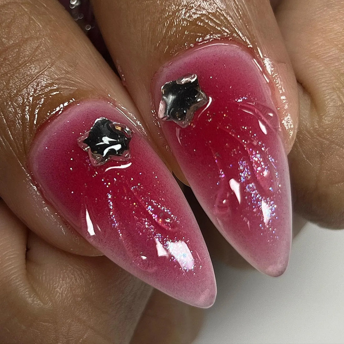 Hand with long stiletto press-on nails in black, red, and chrome, featuring bows, stars, crosses, and 3D accents.