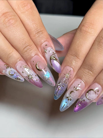 Hand with stiletto press-on nails featuring iridescent ombre, gold moon and star celestial designs.