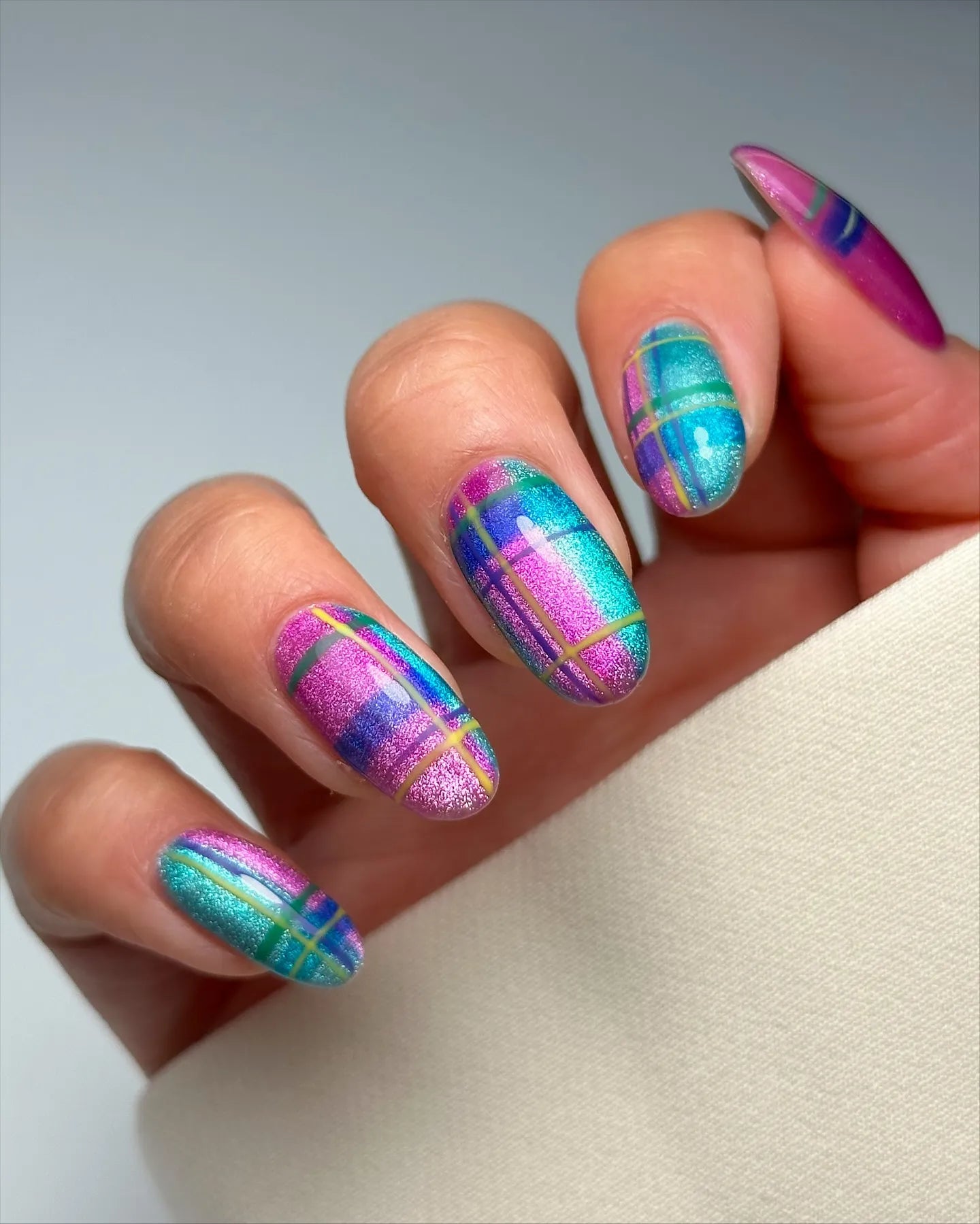 Hand with handmade iridescent neon plaid cat-eye shimmer press-on nails in blue and purple.