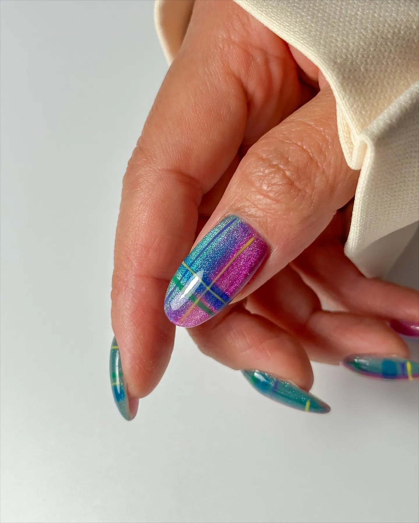 Hand wearing iridescent neon plaid cat-eye shimmer press-on nails