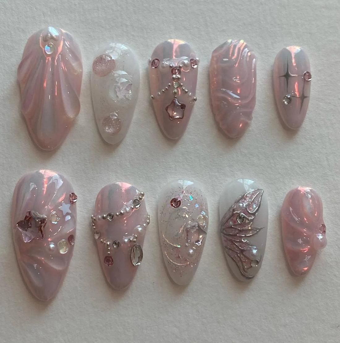 Handmade iridescent pearl pink press-on nails with butterfly, rhinestone, and star accents
