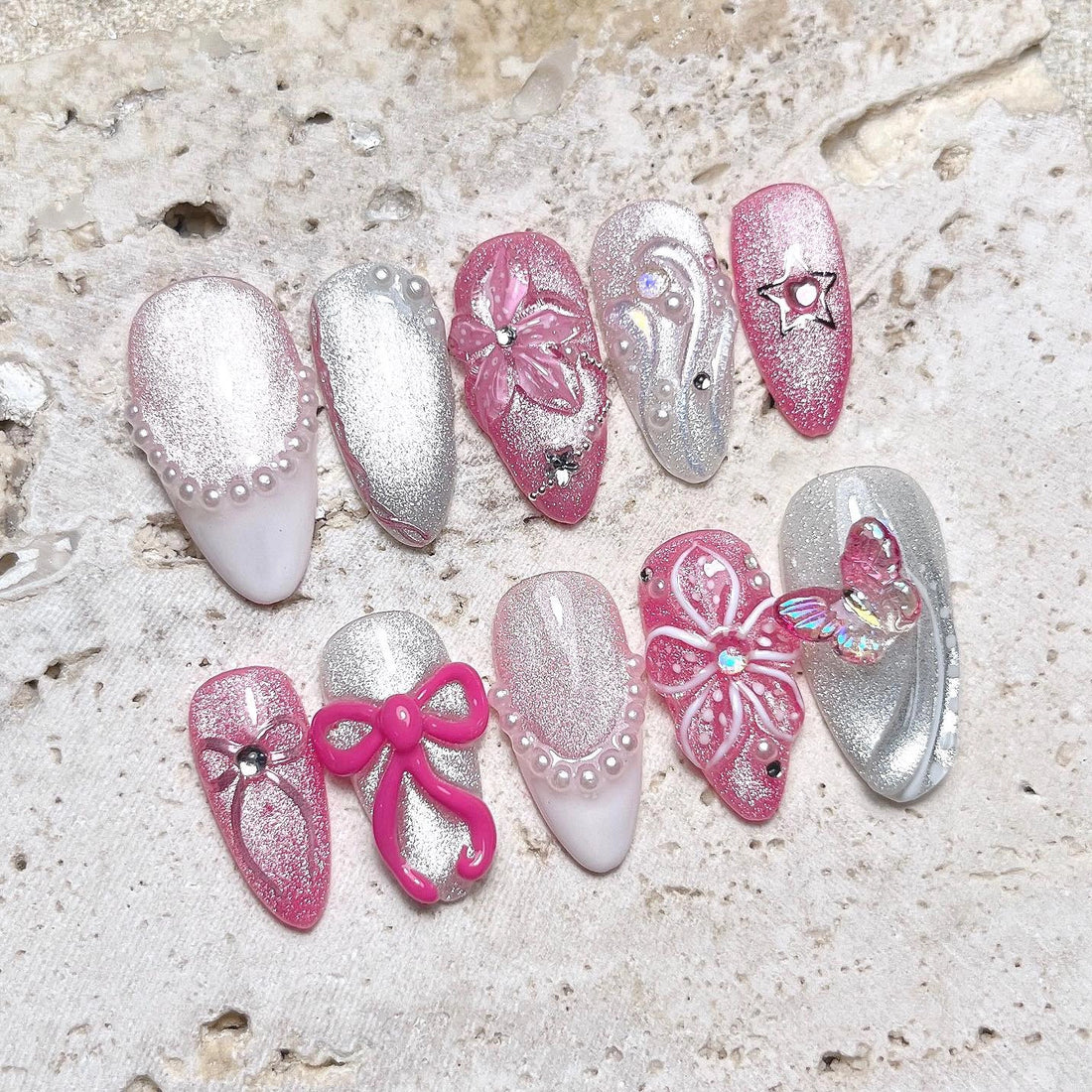 Handmade pink and silver press-on nails with 3D flowers, pearls, bows, and butterfly accents.