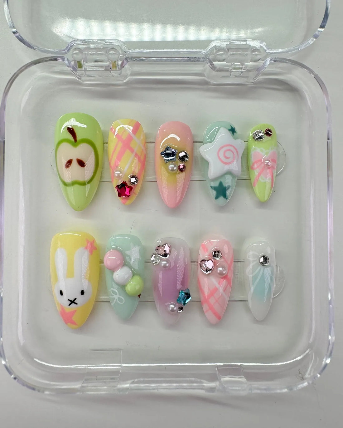 Handmade pastel press-on nails with bunny, apple, star, plaid, bows, and gem accents.
