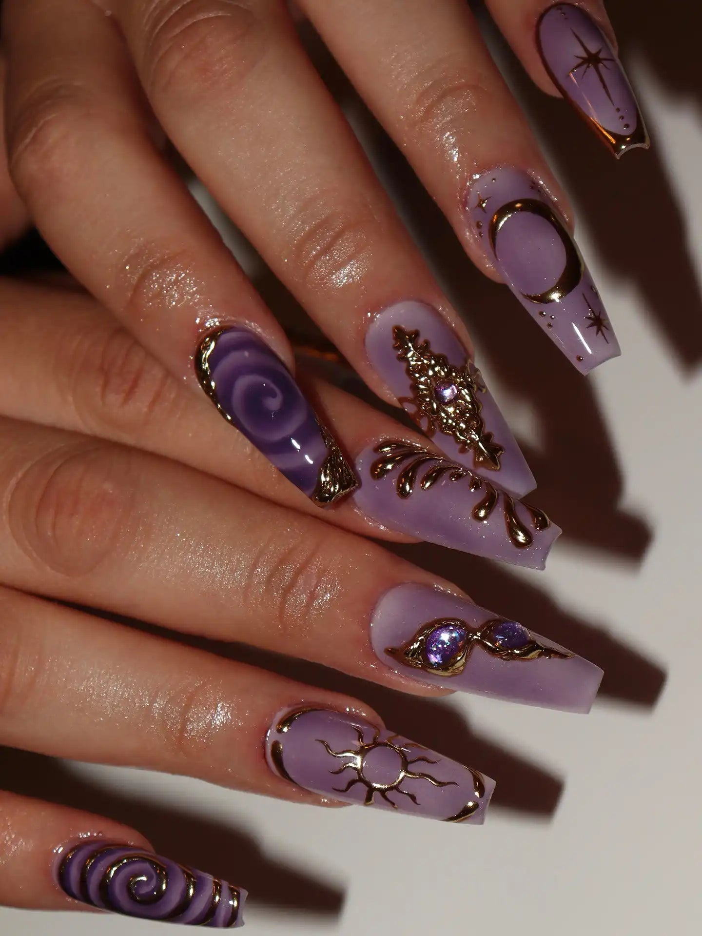 Hand displaying lavender press-on nails with gold celestial moon, sun, and star designs.
