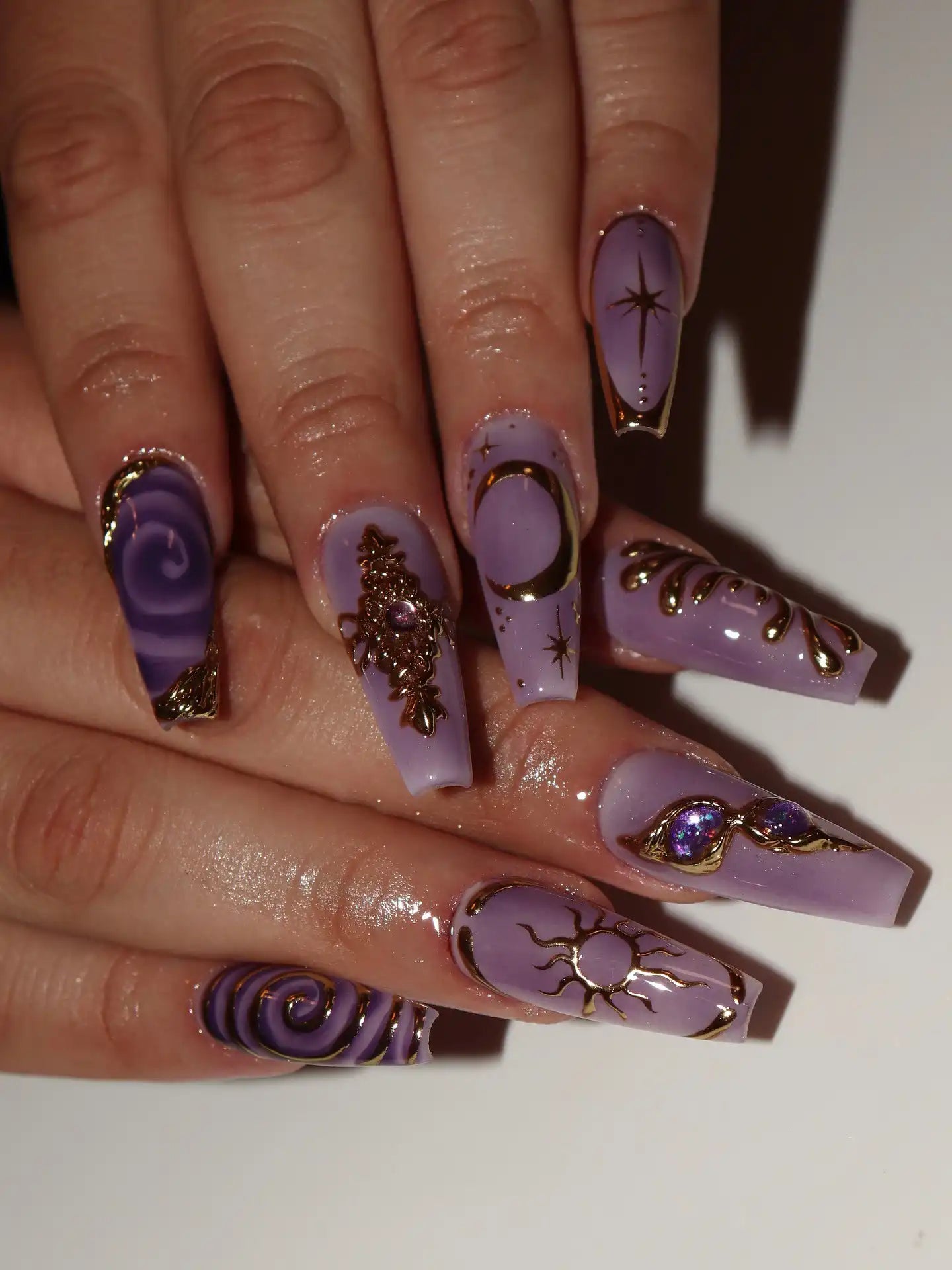 Hand with long lavender press-on nails featuring gold celestial moon, sun, and star designs