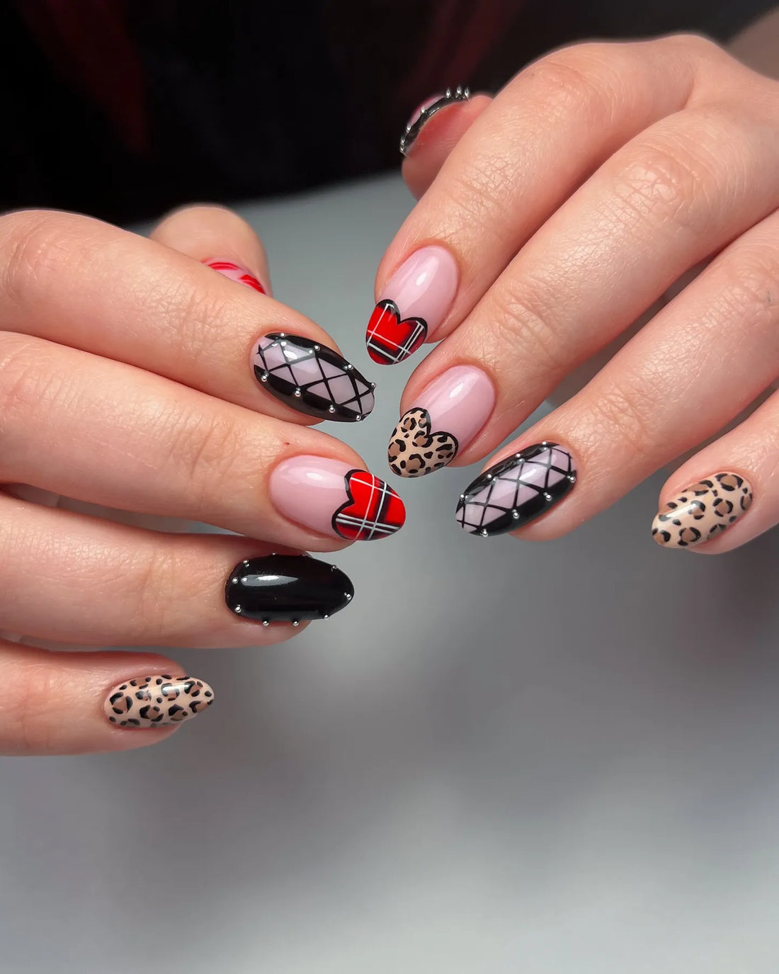 Handmade press-on nails with leopard print, red plaid hearts, black gothic studs, and French tips.