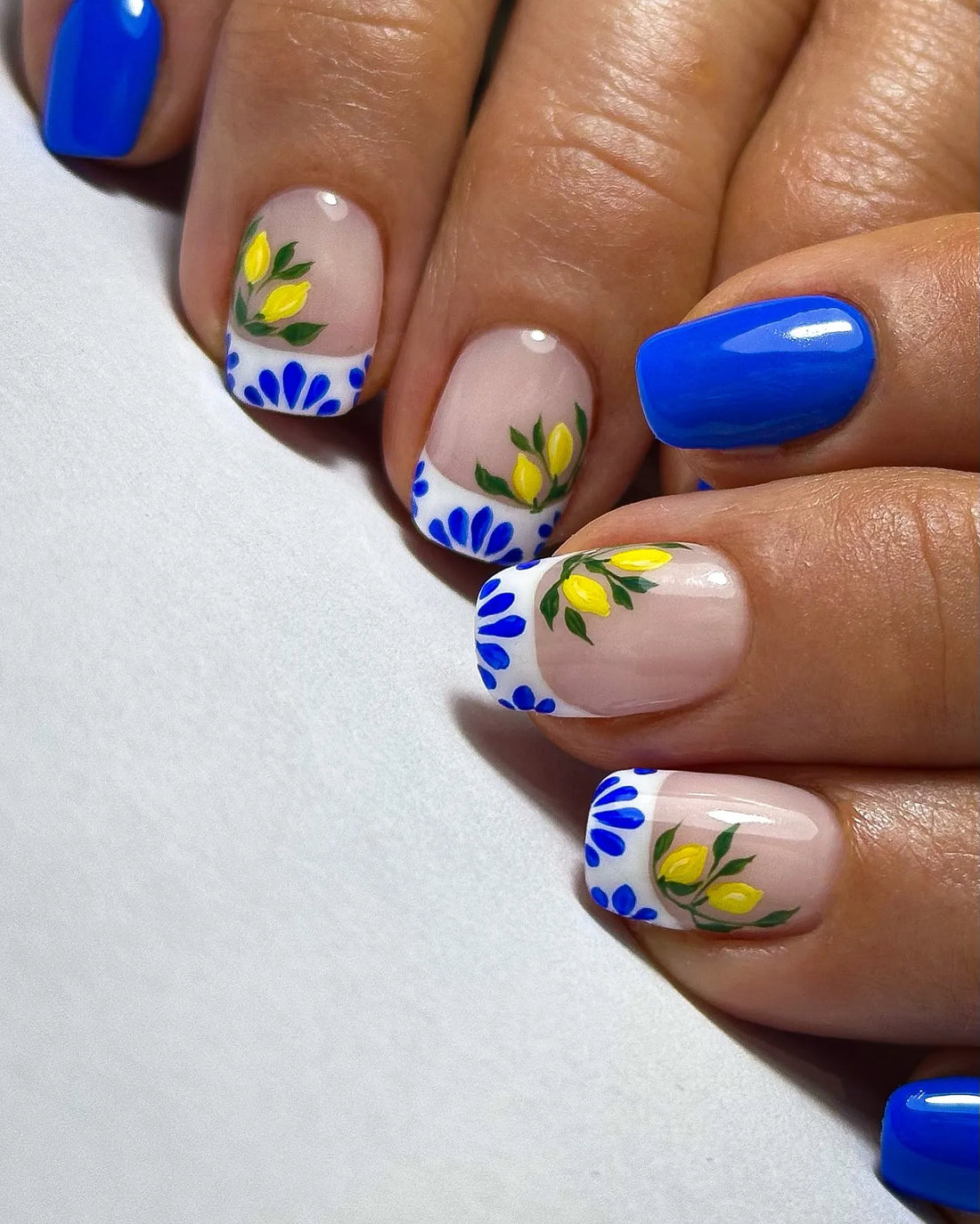Handmade press-on nails with blue French tips, Mediterranean lemon and floral tile design.