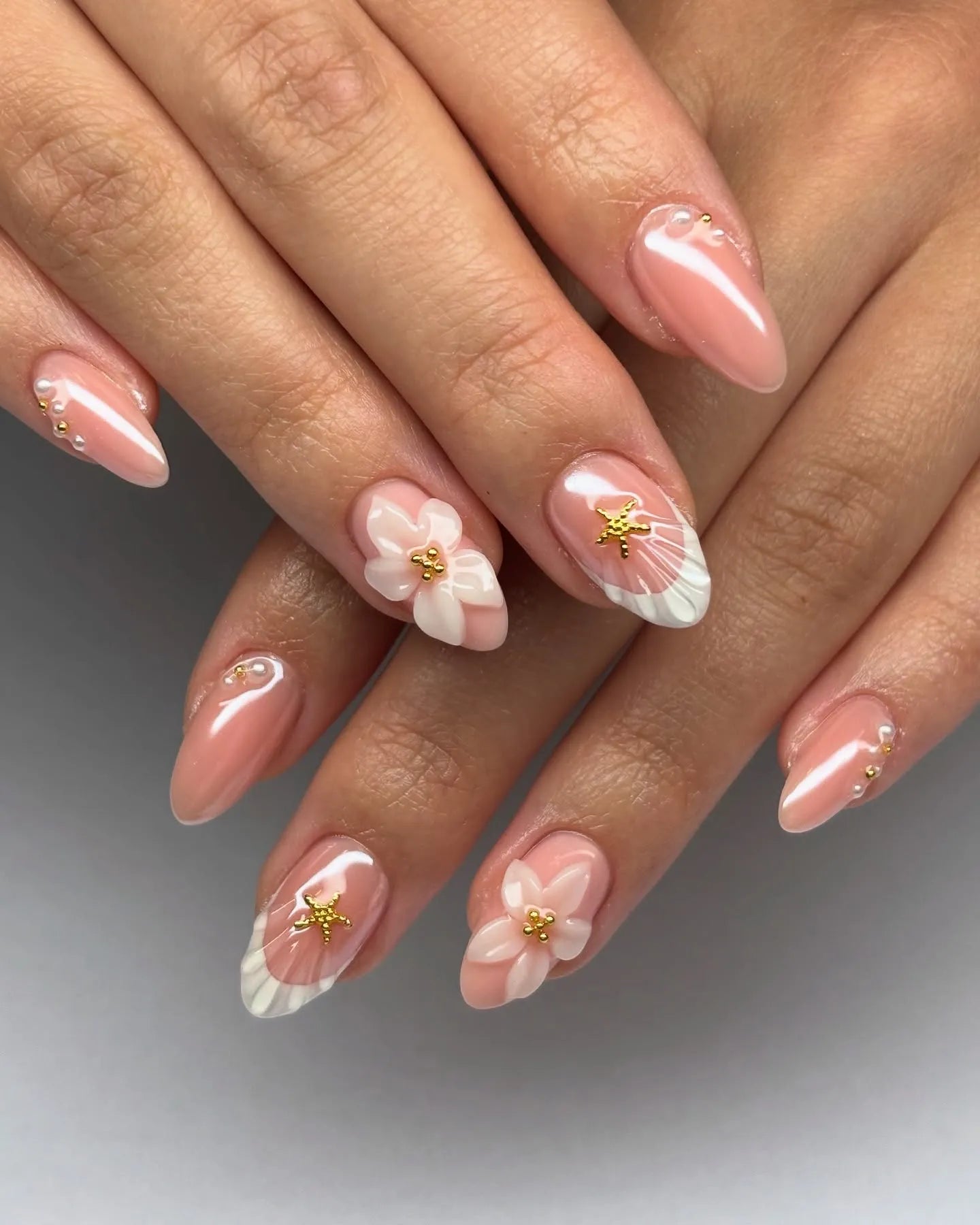 Hand with pink press-on nails featuring 3D white flowers, gold star accents, and pearl details.