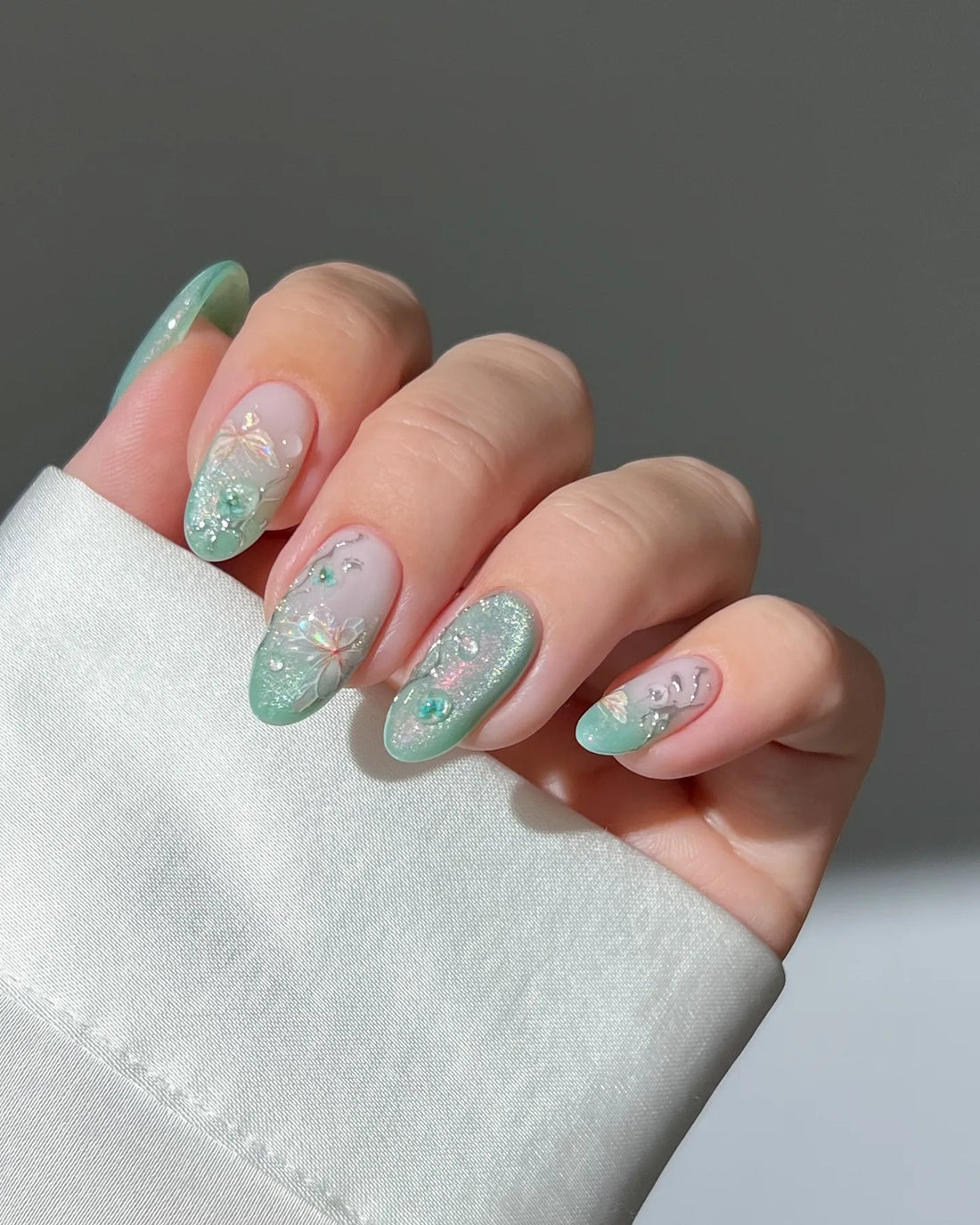 Hand with mint green ombre press-on nails featuring 3D butterfly, floral, and glitter accents.