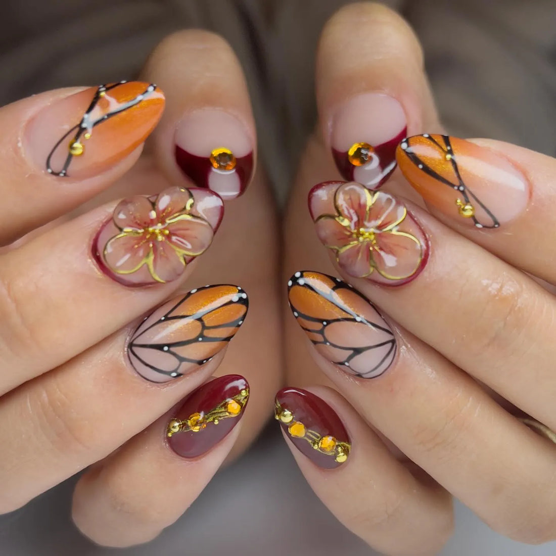 Handmade almond press-on nails with monarch butterfly wing designs, floral accents, and amber gems.