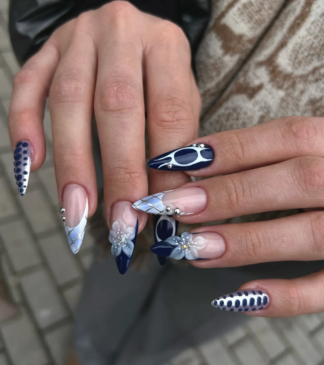 Hand with handmade navy blue, white, and silver press-on nails, featuring floral and marble abstract designs.
