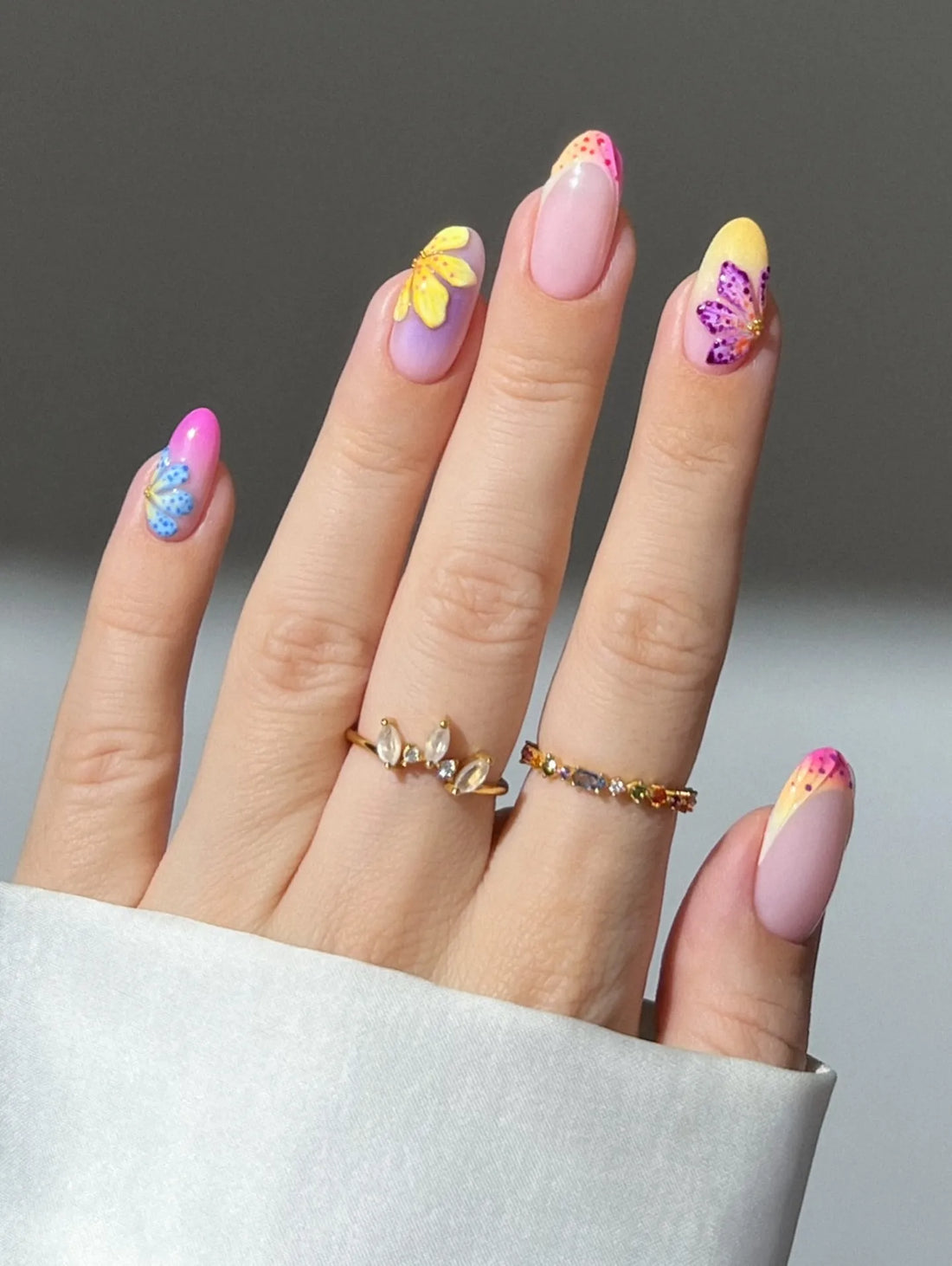 Hand with handmade neon ombre French tip press-on nails featuring summer floral designs