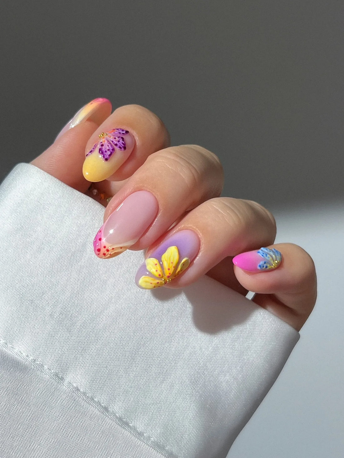 Hand with handmade neon ombre French tip press-on nails featuring summer floral designs