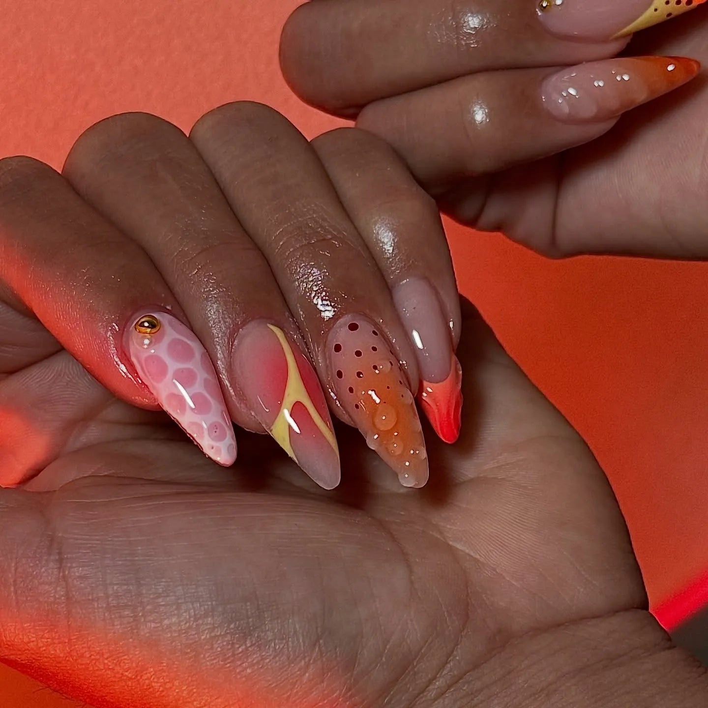 Hand with handmade mismatched neon orange and pink abstract summer press-on nails
