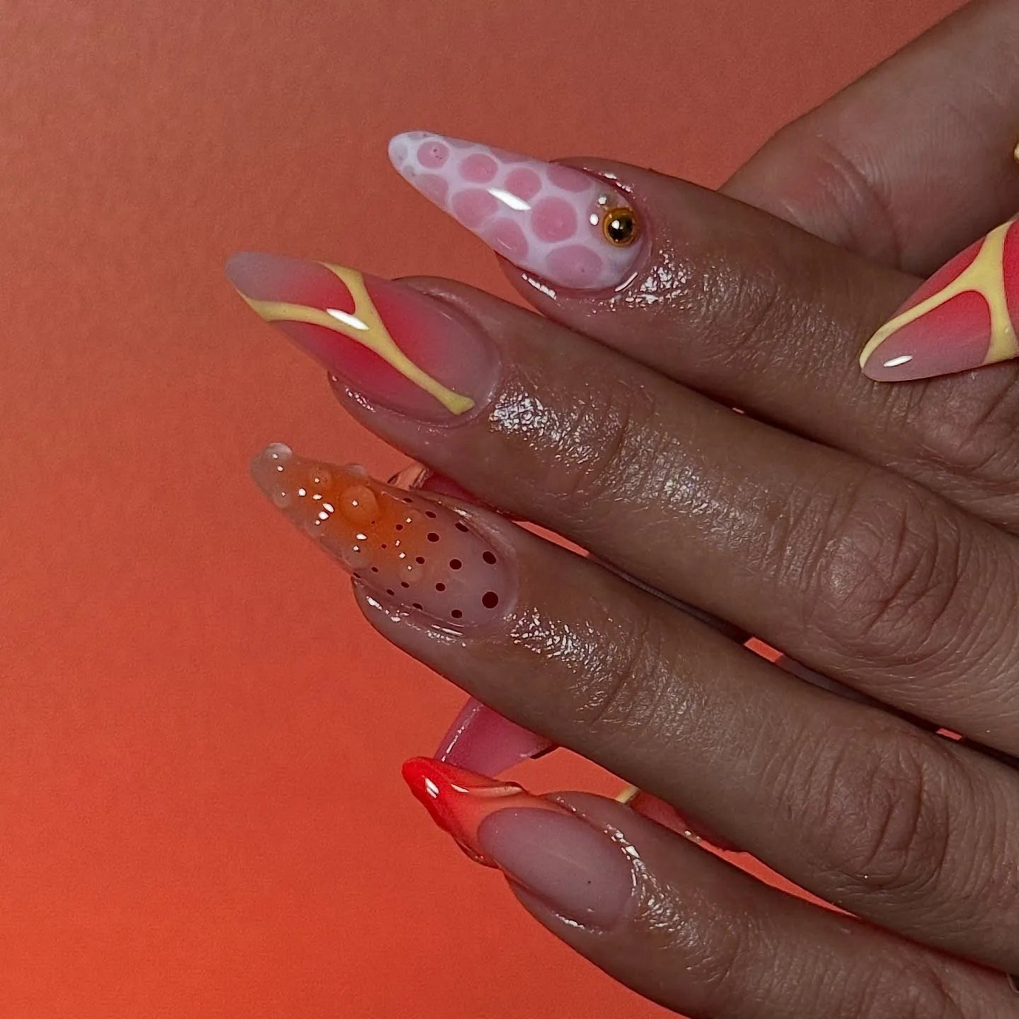 Hand with handmade neon orange and pink butterfly abstract press-on nails, mismatched designs