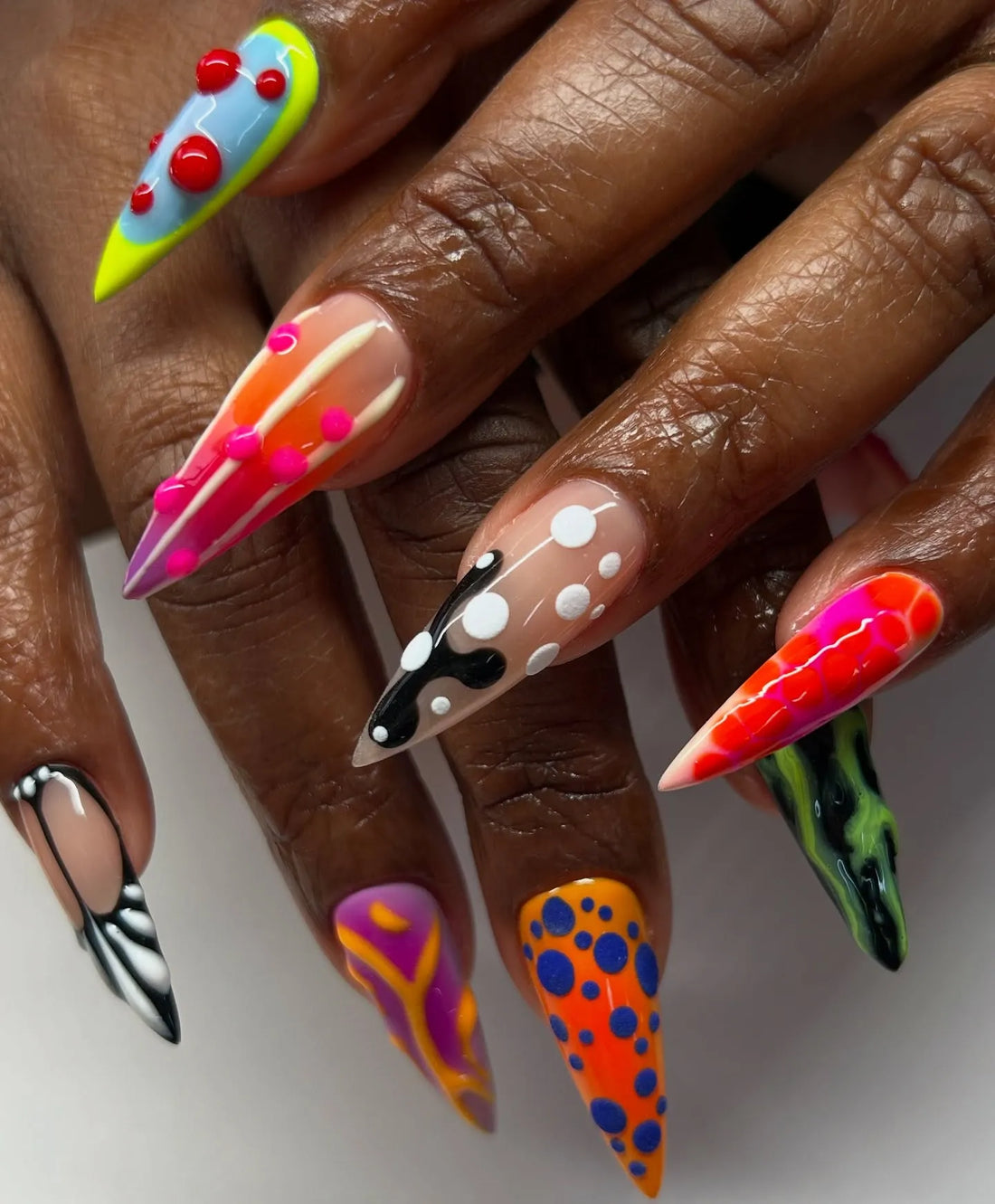Hand with long stiletto press-on nails, featuring bold abstract neon patterns and 3D textures