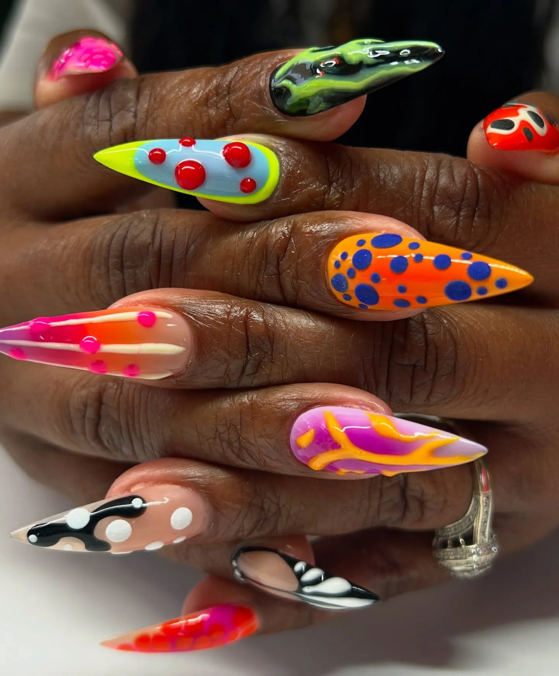 Hand with long stiletto press-on nails, featuring bold abstract neon patterns and 3D textures
