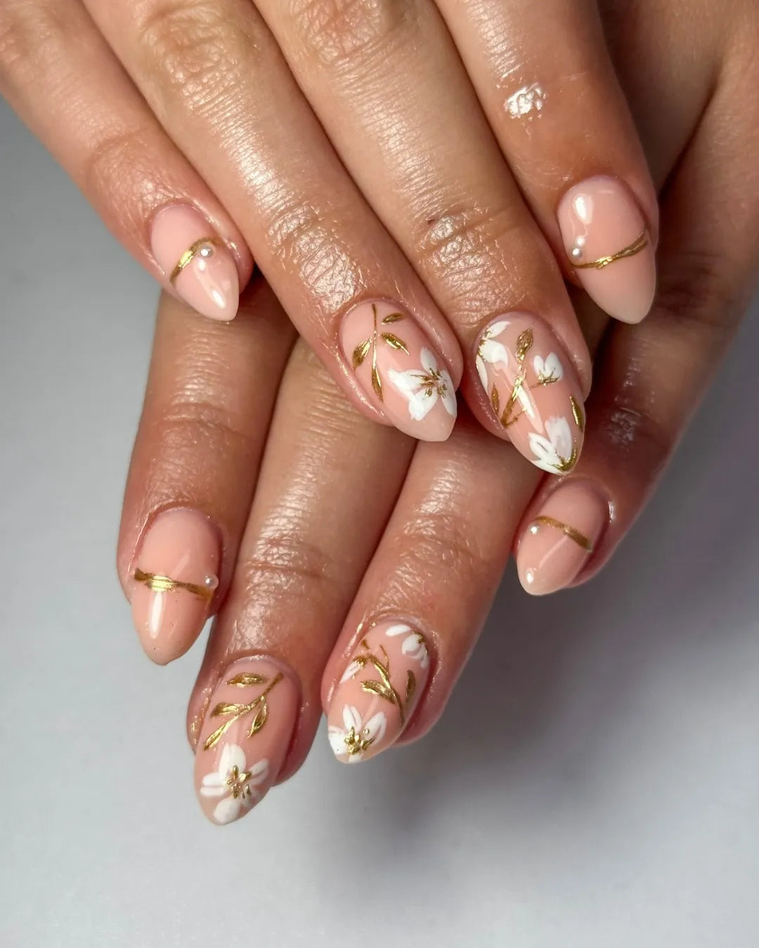 Hand with oval nude press-on nails featuring white floral and gold vine minimalist wedding design