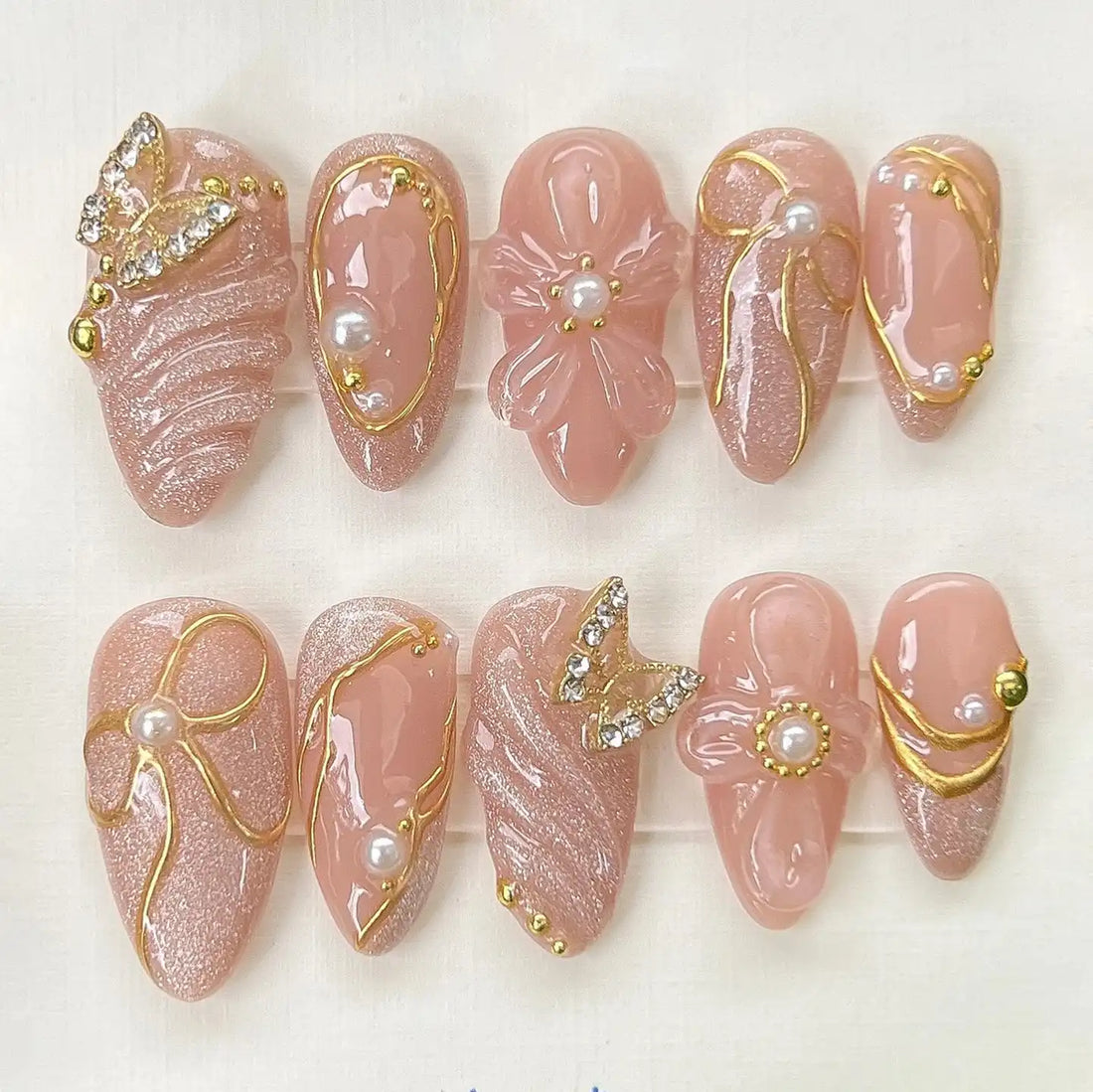Handmade nude glitter press-on nails with pearl, butterfly charms and gold accents, elegant design