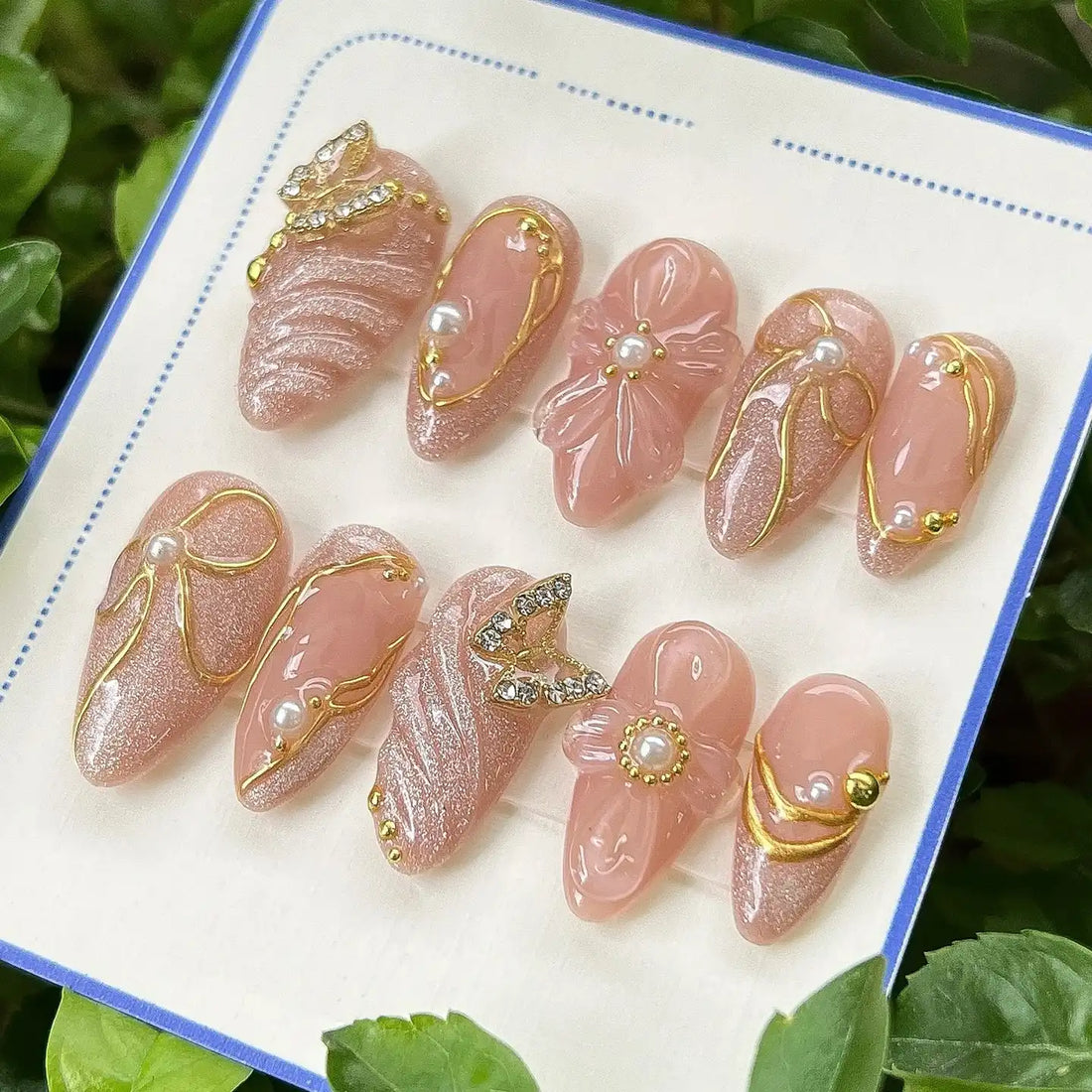 Handmade nude glitter press-on nails with pearl, butterfly charms and gold accents, elegant design