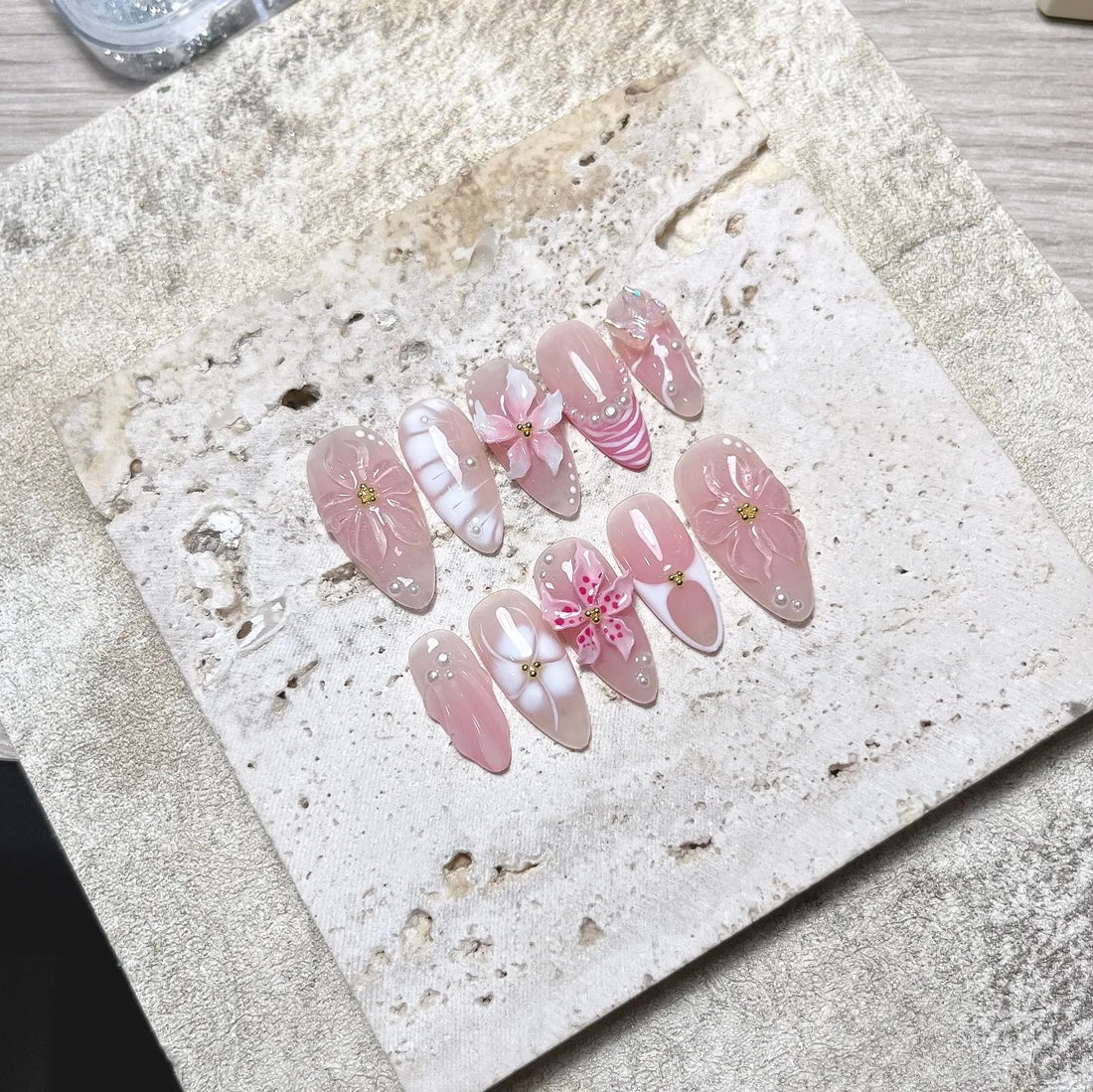 Handmade nude pink press-on nails with 3D petal flowers, pearls, and butterfly accents.