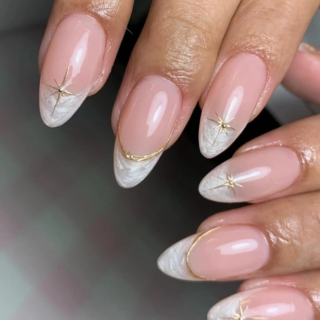 Hand with nude stiletto press-on nails, white and gold starburst French tip design