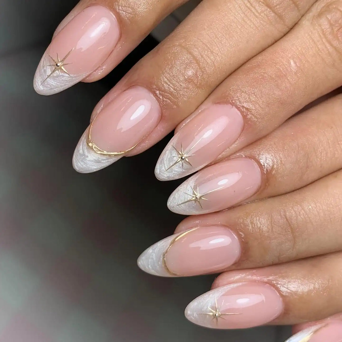 Hand with nude stiletto press-on nails, white and gold starburst French tip design
