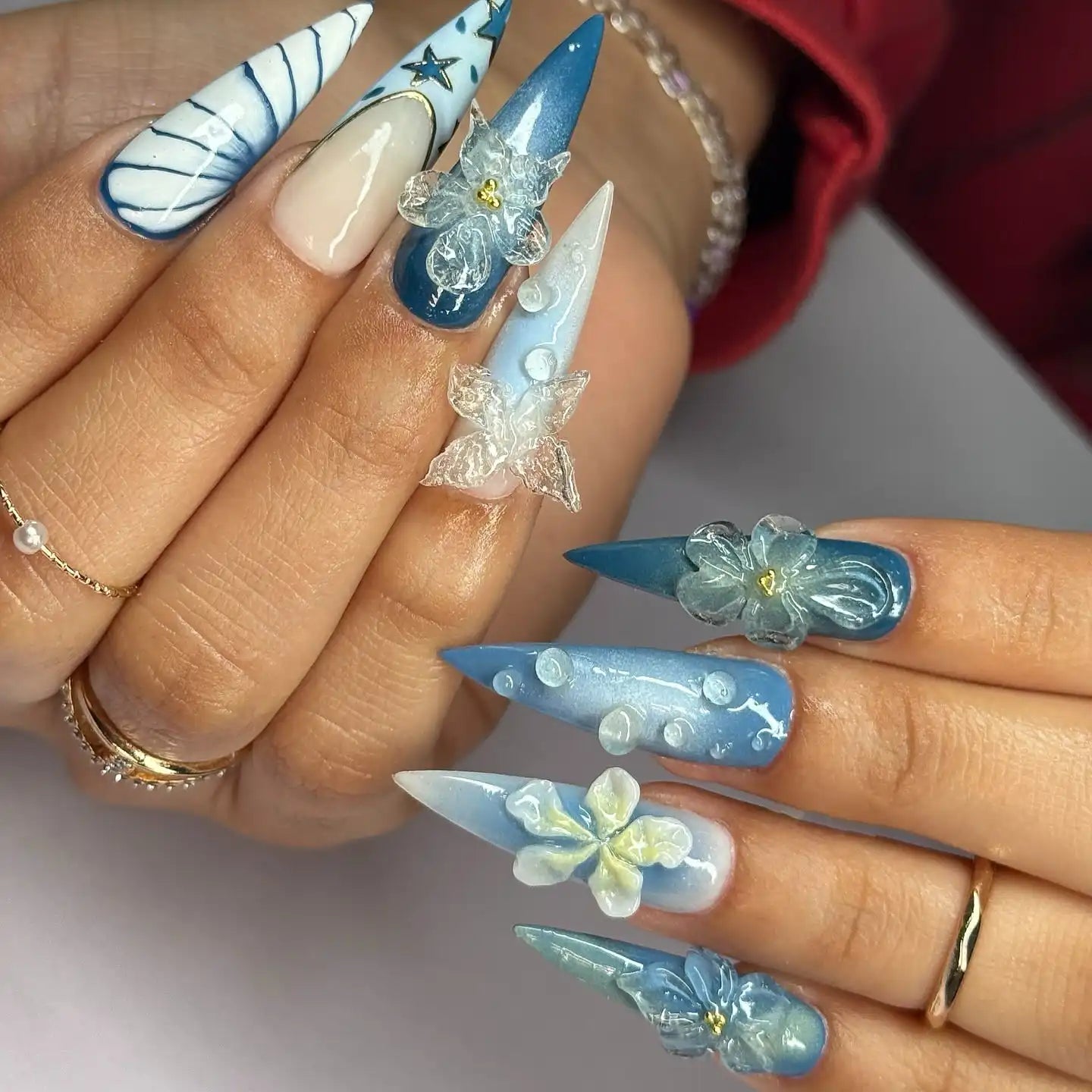 Hand with ocean blue ombre press-on nails featuring 3D floral and butterfly designs.