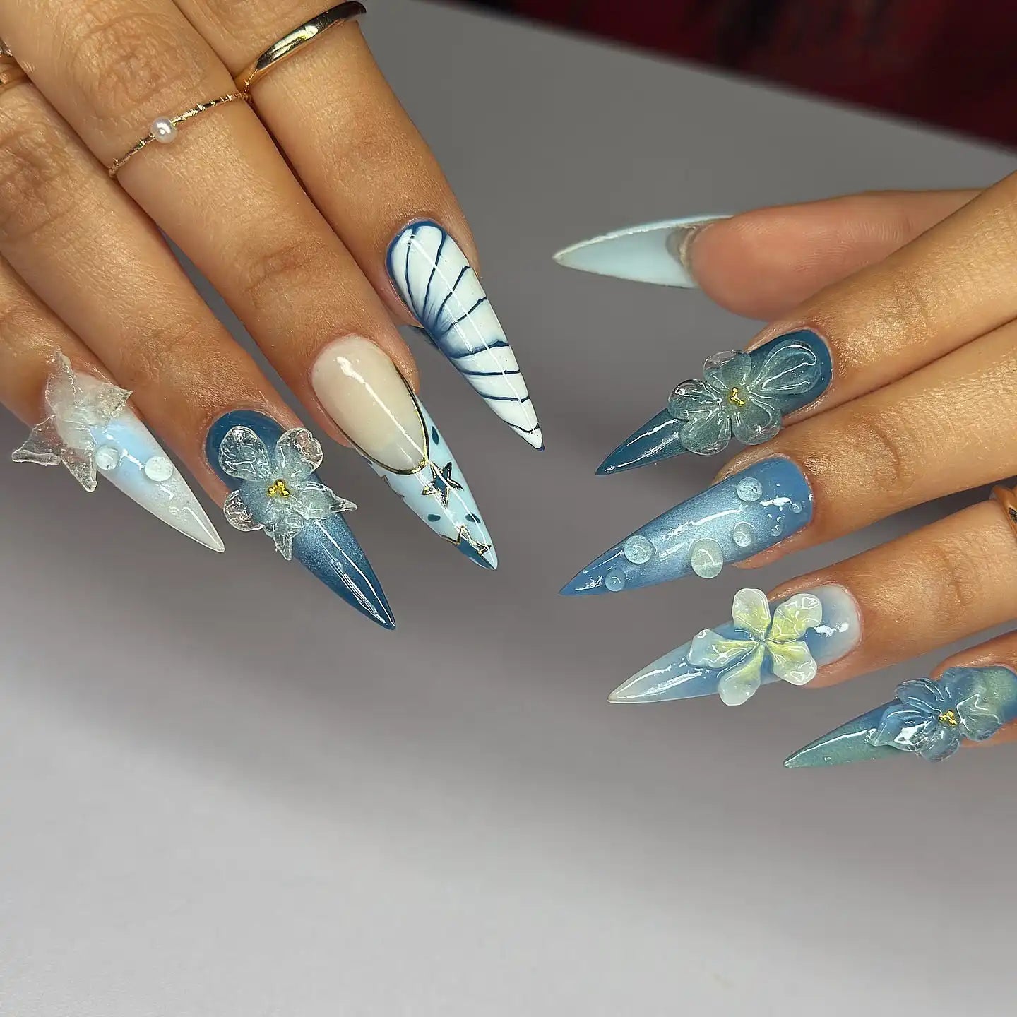 Hand with long stiletto press-on nails in blue ombré, 3D butterfly and floral nail art.