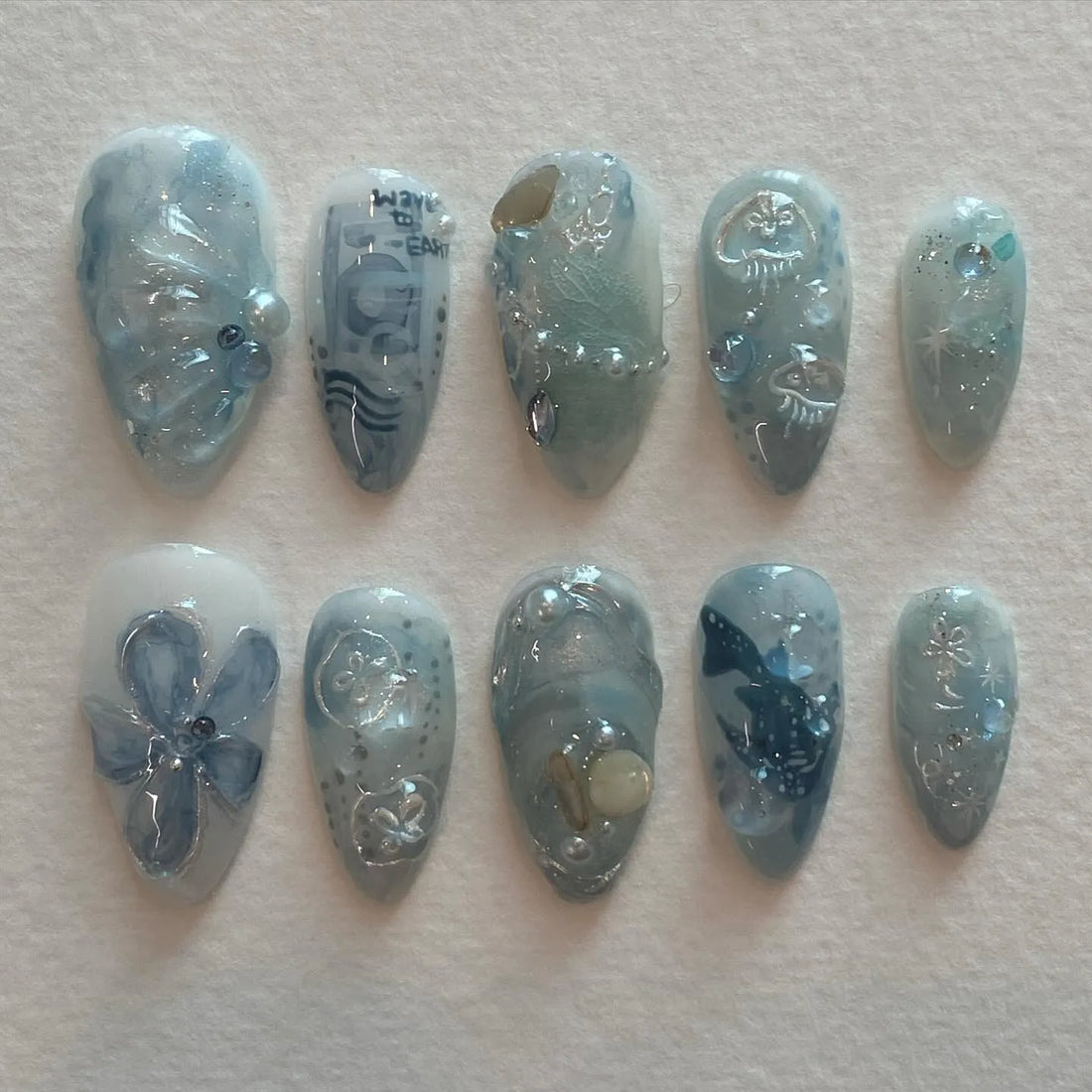 Handmade ocean blue press-on nails with whale, jellyfish, wave, pearl, and sea designs