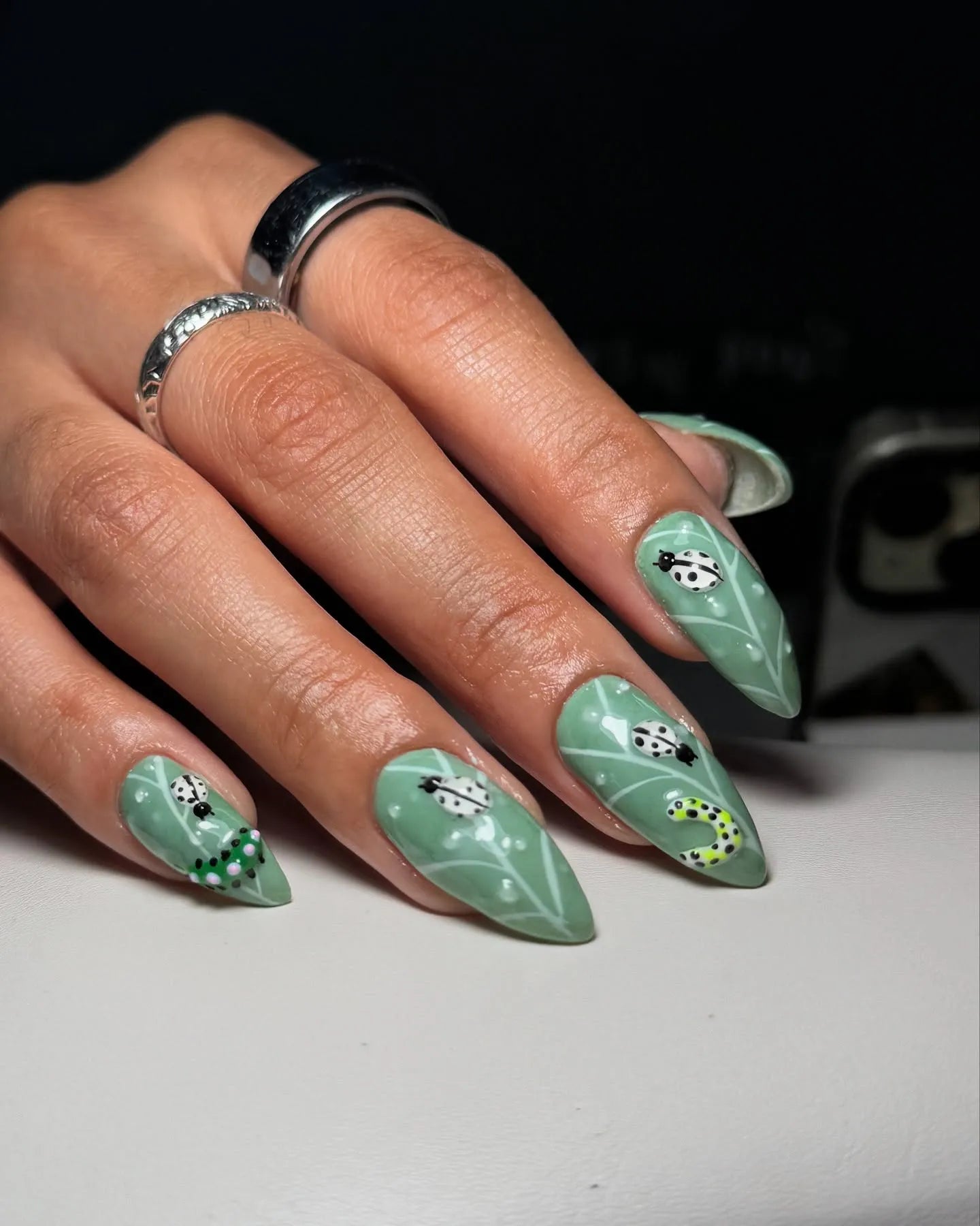 Hand with green nature-themed press-on nails featuring ladybugs and caterpillar art.