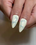 Handmade press-on nails with pale yellow base and blue ribbon designs, almond shape