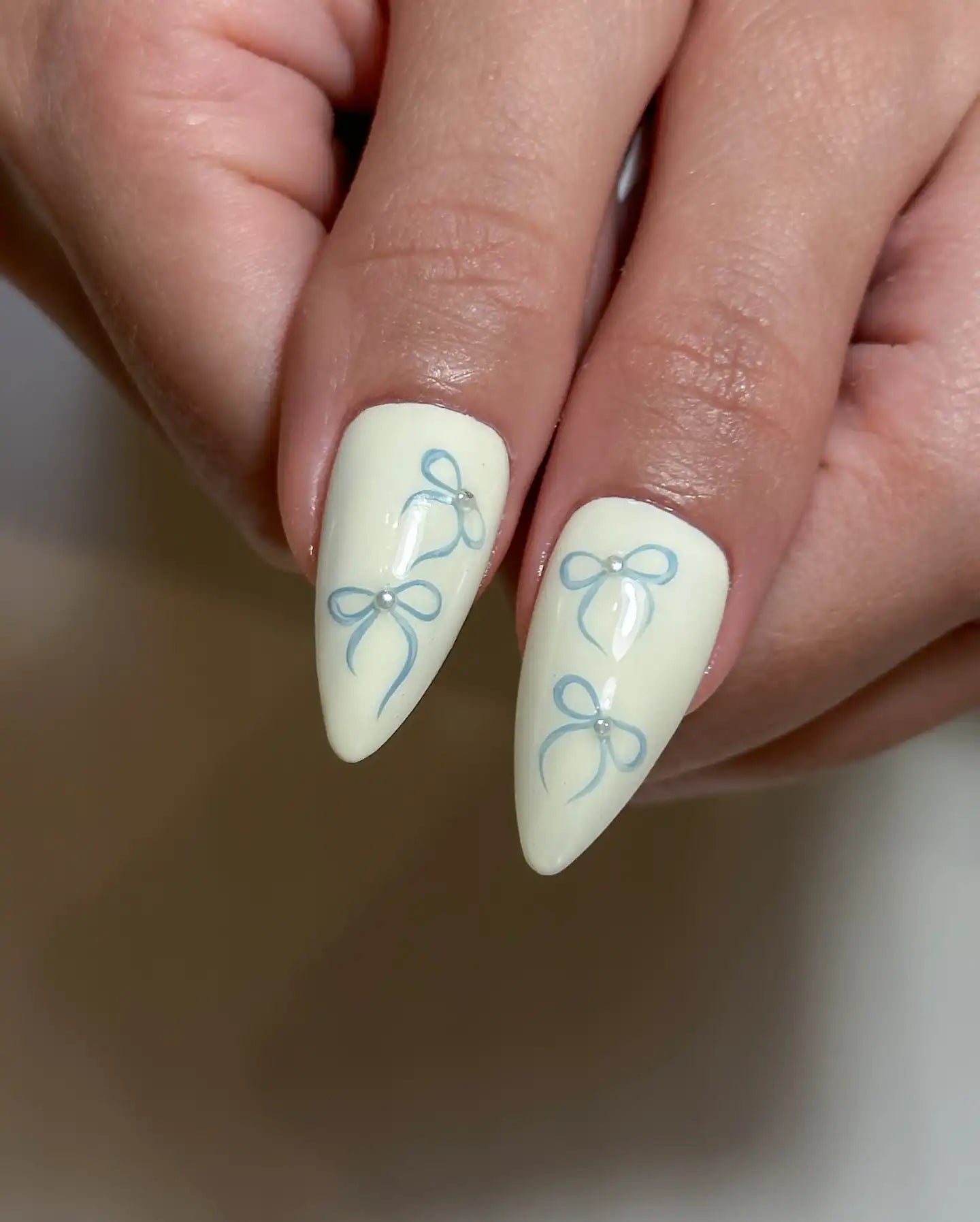 Handmade press-on nails with pale yellow base and blue ribbon designs, almond shape