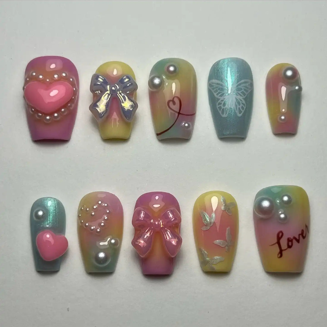 Handmade pastel iridescent press-on nails with 3D heart, bow, butterfly, pearls, and love designs.
